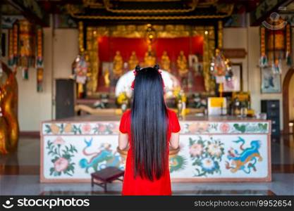beautiful Cute little Asian young woman wearing red traditional Chinese cheongsam decoration Stand for pray to buddha statue for Chinese New Year Festival at Chinese shrine in Thailand