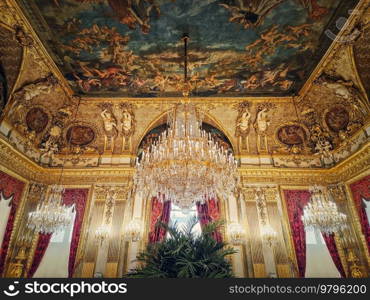 Beautiful decorated Napoleon apartments at Louvre palace. Royal family rooms with cardinal red curtains, golden ornate walls, paintings and crystal chandeliers suspended from ceiling