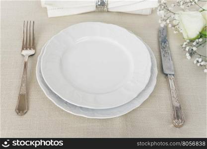 Beautiful decorated table with empty white plates, linen napkin, cutlery and white rose flowers on tablecloths, with space for text