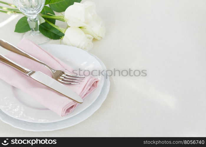 Beautiful decorated table with white plates, crystal glass, linen pink napkin, cutlery and white rose flowers on tablecloths, with space for text