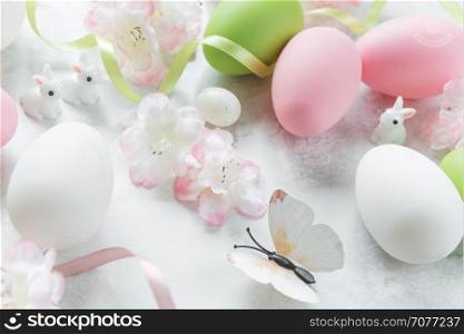 Beautiful delicate Easter composition with pink cherry flowers, multicolored Easter eggs, Easter bunny and butterfly on the stone background