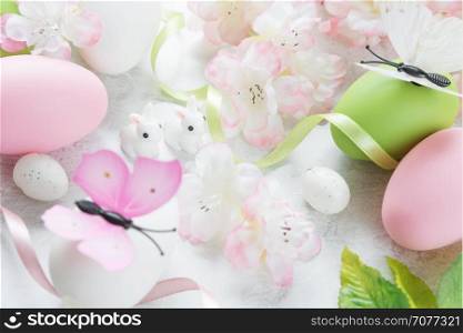 Beautiful delicate Easter composition with pink cherry flowers, multicolored Easter eggs, Easter bunny and butterfly on the stone background