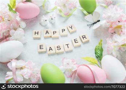 "Beautiful delicate Easter composition with pink cherry flowers, multicolored Easter eggs, Easter bunny, butterfly and inscription "Happy Easter" on the stone background"