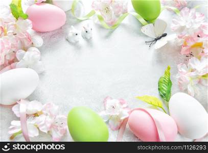 Beautiful delicate Easter frame with pink cherry flowers, multicolored Easter eggs, Easter bunny and butterfly on the stone background, with copy-space