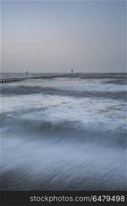 Beautiful dramatic stormy landscape image of waves crashing onto. Beautiful moody stormy landscape image of waves crashing onto beach at sunrise