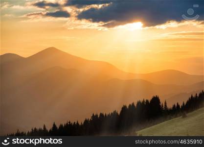 Beautiful dramatic sunset in the mountains. Landscape with sun shining through orange clouds