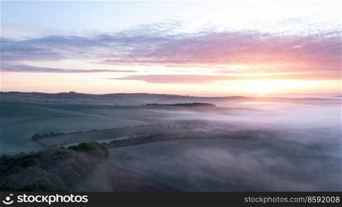 Beautiful drone landscape image of sea of fog rolling across South Downs English countryside during Spring sunrise