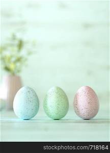 Beautiful Easter eggs decorated in blue, green and pink colors, balanced vertically on its blunt end on cyan background with copy space for your holiday greeting in square format