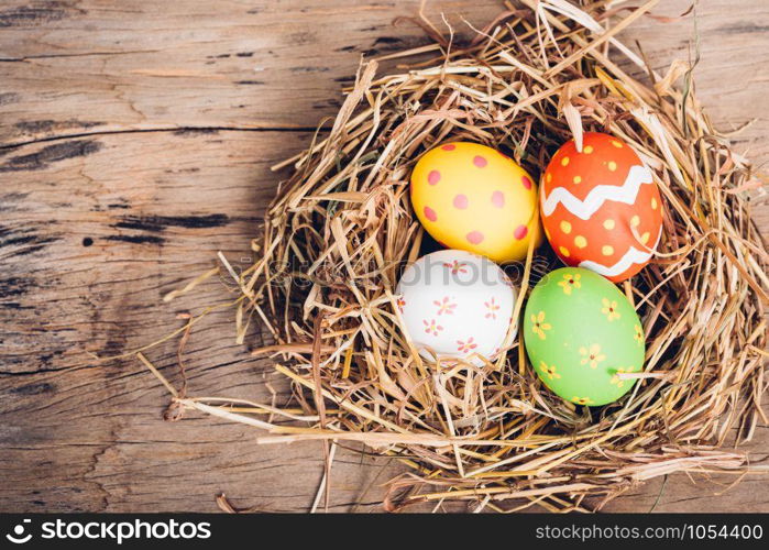Beautiful Easter multi color egg in straw on wooden background, Easter day concept