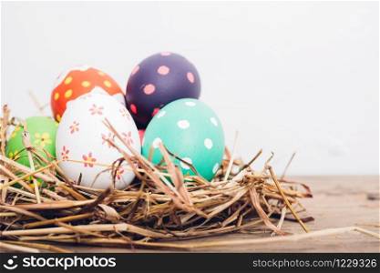 Beautiful Easter multi color egg in straw on wooden background, Easter day concept