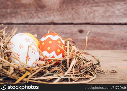 Beautiful Easter multi color egg in straw on wooden background, Easter day concept