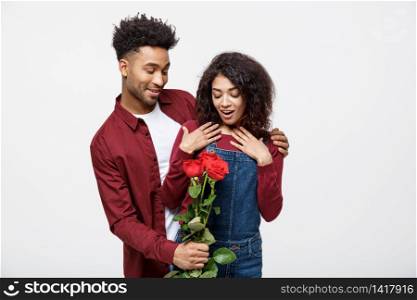 Beautiful elegant couple is hugging and smiling, on gray background. Girl is holding roses.. Beautiful elegant couple is hugging and smiling, on gray background. Girl is holding roses