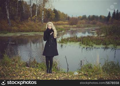 Beautiful elegant woman in a black coat on the river bank