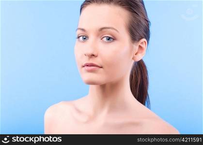 beautiful elegant woman is looking at camera and touching her face on blue background
