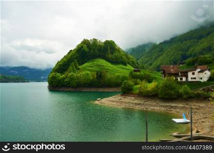Beautiful emerald mountain lake in Switzerland under low clouds