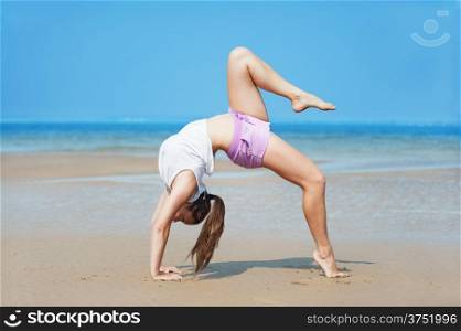 Beautiful energetic young woman doing handstand on the beach