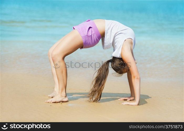 Beautiful energetic young woman doing stretching exercise on the beach