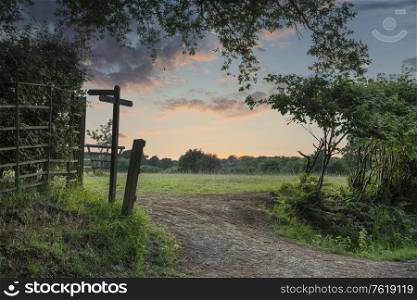 Beautiful English countryside Summer sunset landscape image with footpath signposted through warm field
