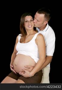 Beautiful expectant mother receiving a kiss from her loving husband. Black background.