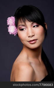 Beautiful face of an Asian-American woman with purple pink white flowers in her hair, looking to her side, isolated.