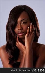 Beautiful face of an attractive African black woman with almond shaped eyes and long wavy hair and hands in her face, isolated.