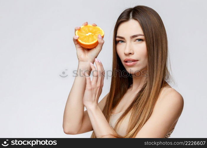 Beautiful Face of Young Woman with Clean Fresh Skin close up. Beauty Portrait. Beautiful Spa Woman Smiling. Perfect Fresh Skin. Pure Beauty Model. Youth and Skin Care Concept. Beautiful Woman with Clean Fresh Skin holding orange