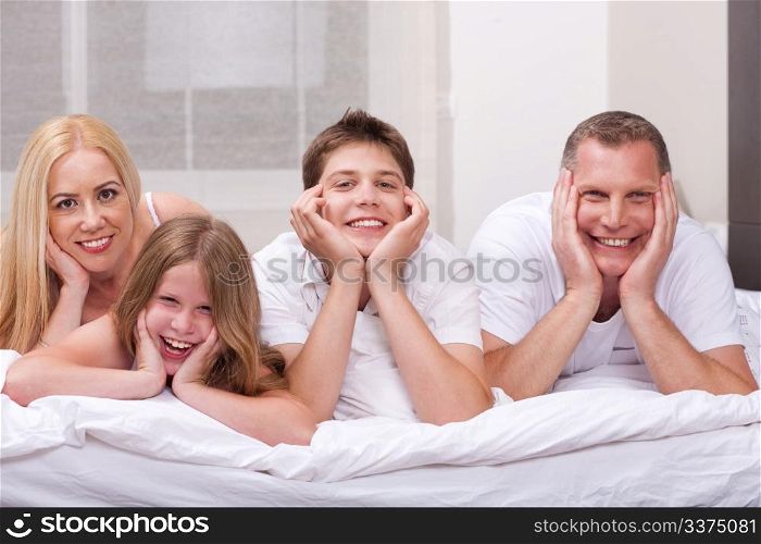 Beautiful family lying on bed smiling and looking at you in living room