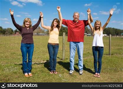 Beautiful family outdoors on their farm holding hands and raising their arms in praise and joy.