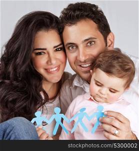 Beautiful family together isolated on gray background, happy young parents carry little daughter, people-shaped blue paper bonding toy in hands, togetherness concept