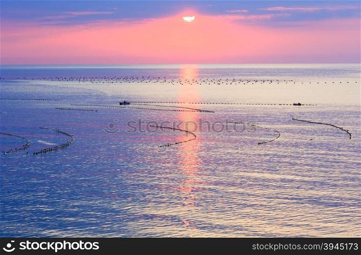Beautiful fascinate morning sea view with sunrise, sun track on surface and fishing nets. People on boats are unrecognizable.