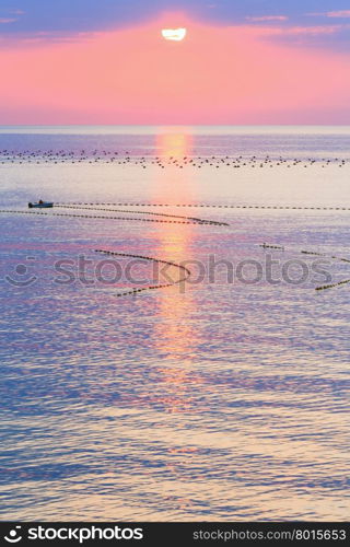 Beautiful fascinate morning sea view with sunrise, sun track on surface and fishing nets. Man on boat is unrecognizable.