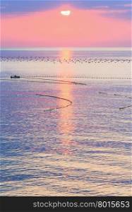 Beautiful fascinate morning sea view with sunrise, sun track on surface and fishing nets. Man on boat is unrecognizable.