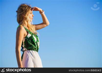 Beautiful fashion model against blue clear sky looking in distance gesturing with hands, sunlight.. Fashionable woman looking in distance