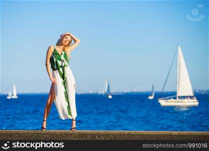 Beautiful fashion model against sea. Pretty blonde young adult woman wearing long white green summer dress.. Woman in summer long dress against sea