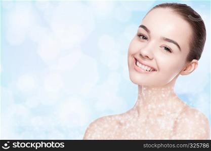 Beautiful fashion model girl with cute smile natural makeup spa skin care portrait on blue bokeh background with shiny glitter stars on neck