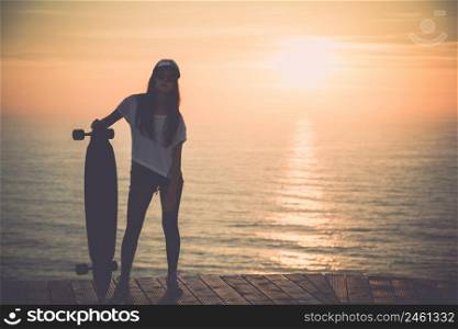 Beautiful fashion skater girl posing with a skateboard at the sunset
