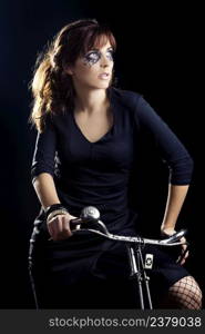 Beautiful fashion woman posing with a old bicycle over a black background