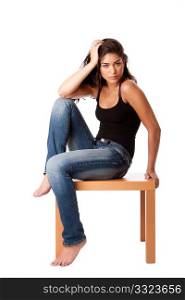 Beautiful fashion woman sitting on wooden table wearing blue denim jeans and black tank top, isolated.