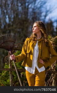 Beautiful fashionable woman and rake in the garden, springtime