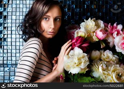 Beautiful fashionable woman portrait indoors at vintage luxury interior. She is standing near bouquet of beautiful flowers