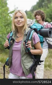 Beautiful female backpacker looking away with man standing in background at forest