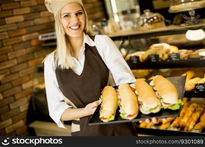 Beautiful female bakery posing with various types of sandwiches in the baker shop