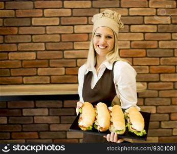 Beautiful female bakery posing with various types of sandwiches in the bakery shop