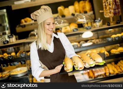 Beautiful female bakery posing with various types of sandwiches in the bakery shop