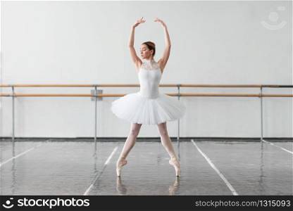 Beautiful female ballet dancer in ballet class, barre and white wall on background. Beautiful female ballet dancer in class