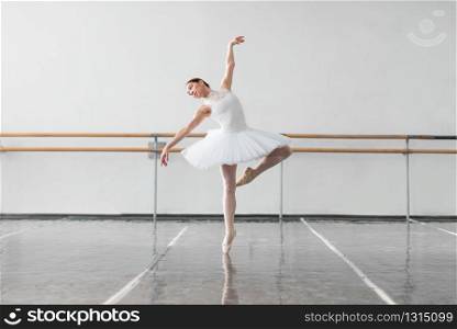 Beautiful female ballet dancer keep the rack in ballet class, barre and white wall on background