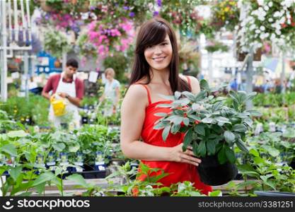 Beautiful female customer holding potted plant with workers in background