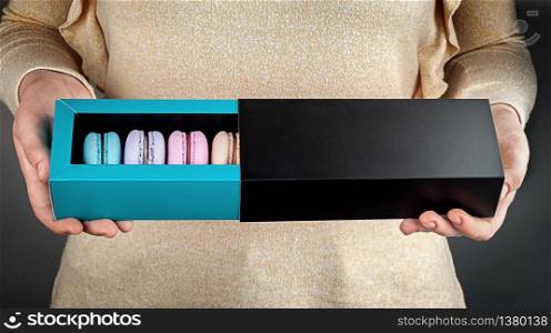 Beautiful female hands hold multicolored french macaroons in gift box. Girl holding open box with macaroons