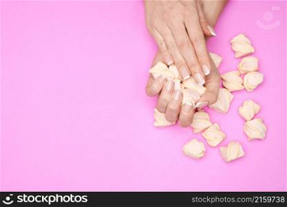 Beautiful Female Hands with French manicure and marshmallows over colorful pink paper background,. Beautiful Female Hands with French manicure and marshmallows over colorful pink paper background