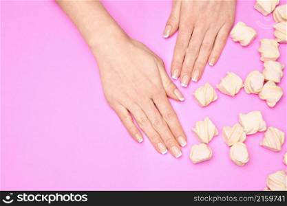 Beautiful Female Hands with French manicure and marshmallows over colorful pink paper background,. Beautiful Female Hands with French manicure and marshmallows over colorful pink paper background